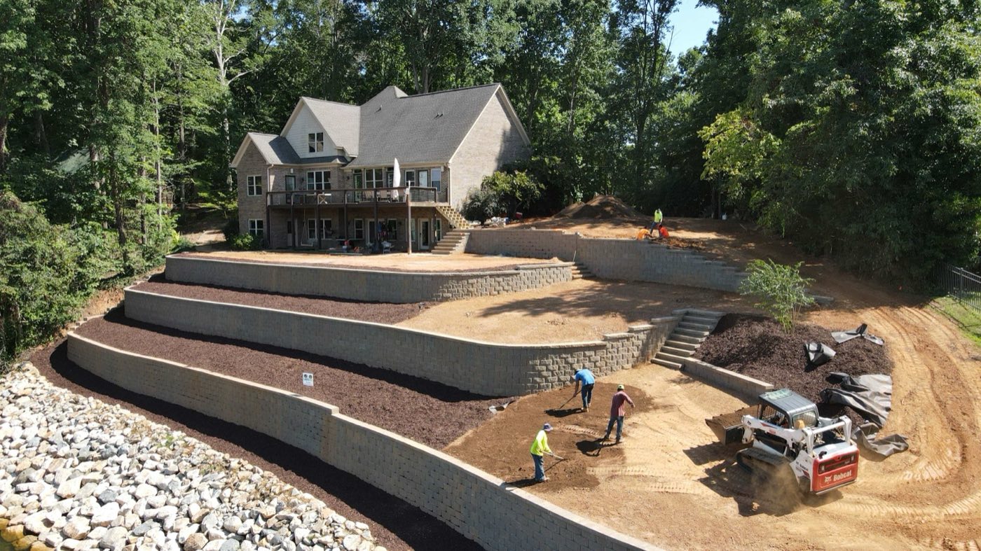 Crew and skid steer finishing tiered block retaining walls behind a Mooresville home