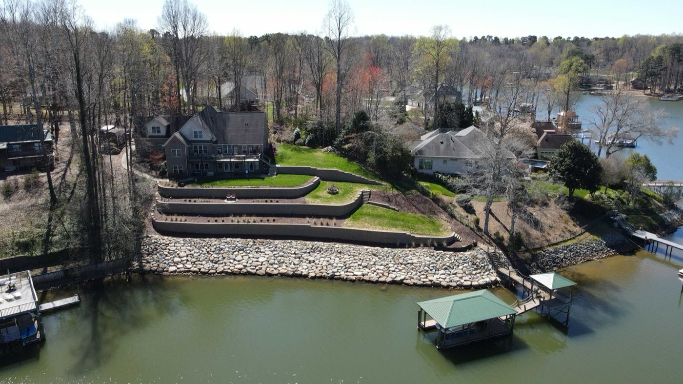 Aerial of tiered retaining walls stepping a lakefront lawn down toward a covered dock