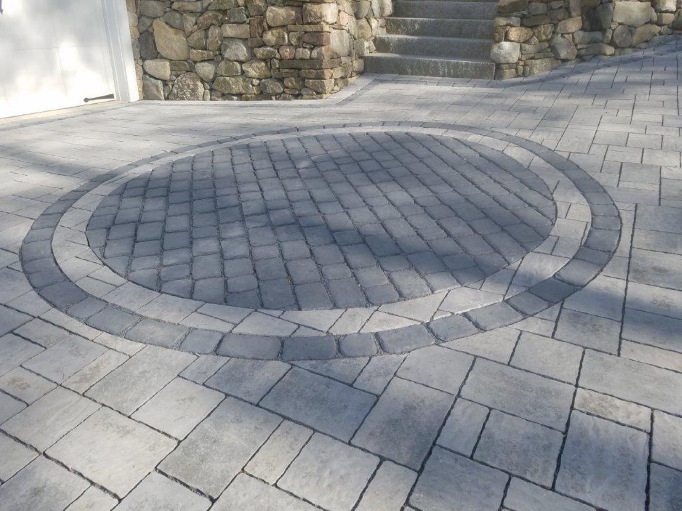 Grey paver driveway with a circular cobble inlay set inside a contrasting ring border