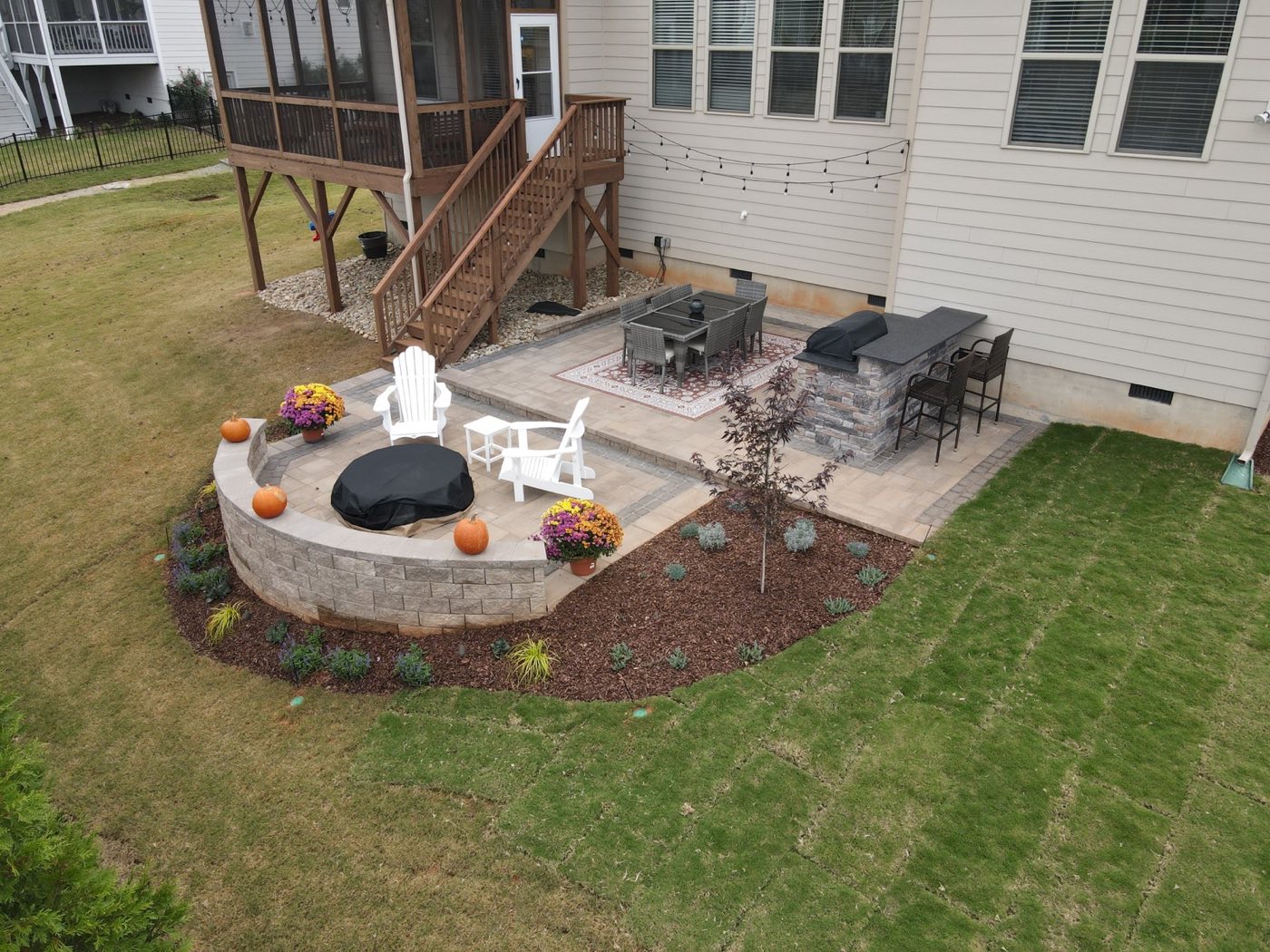 Aerial of a paver patio with a curved seat wall, fire pit and bar, dressed for autumn