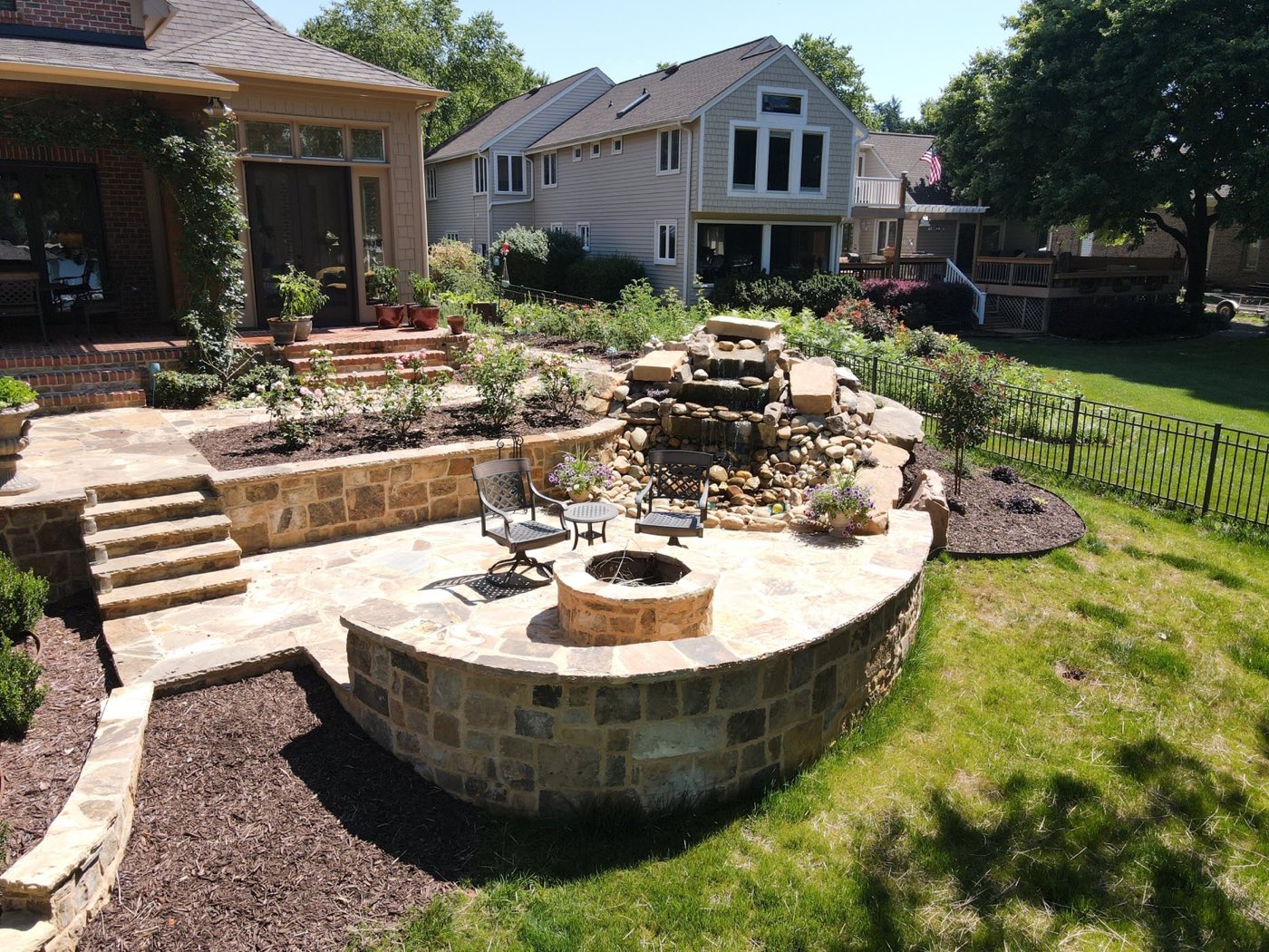 Multi-level stone patio with a round fire pit, curved seat wall and a boulder waterfall alongside