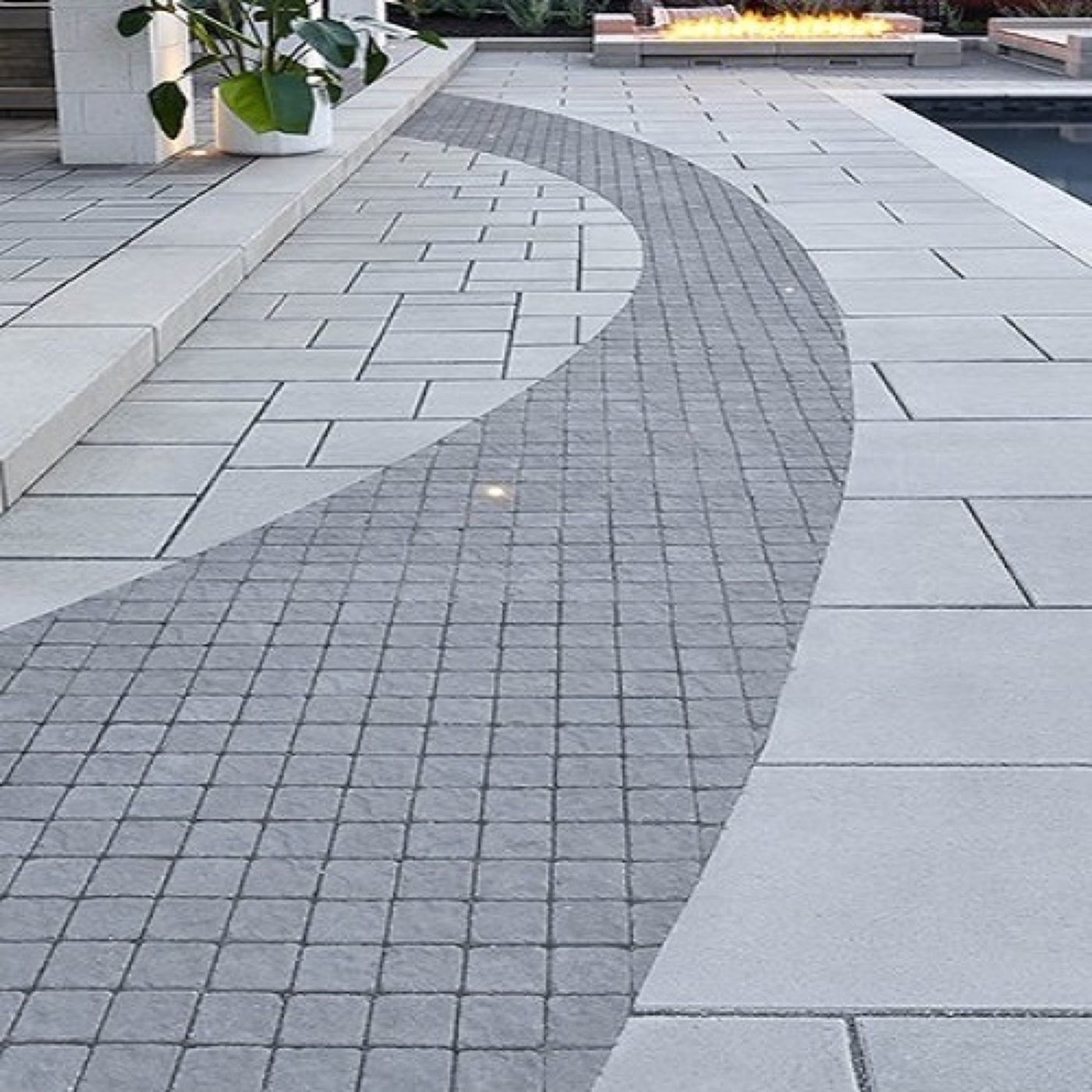 Grey slab patio with a sweeping curve of cobble setts inlaid between the pool and fire feature