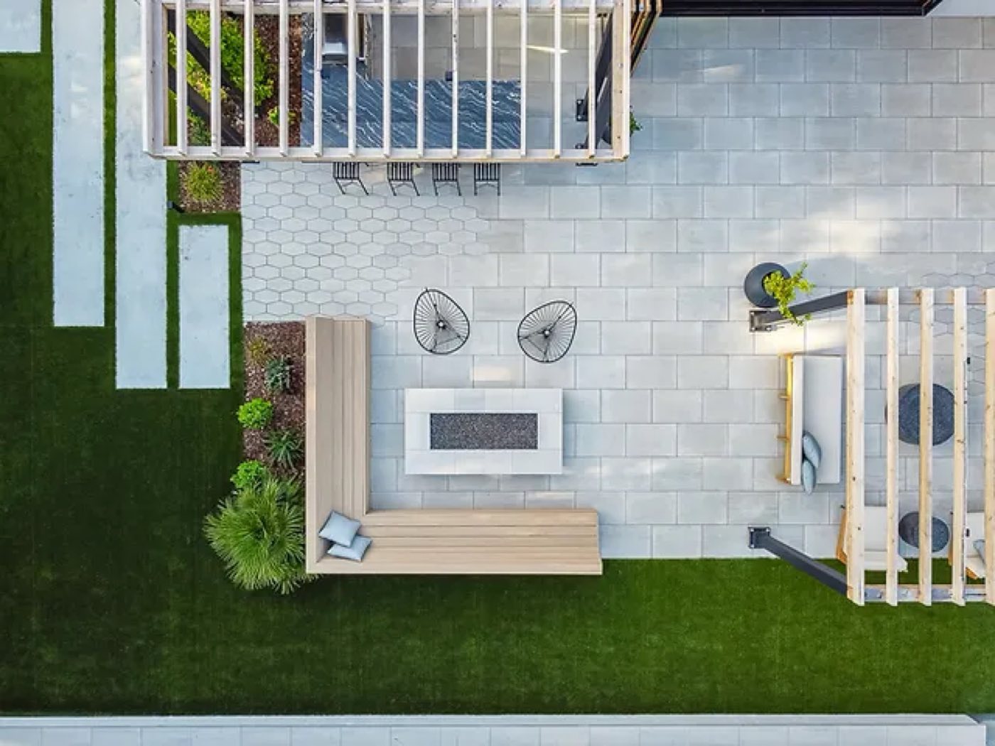 Overhead of a modern courtyard mixing grey slabs, turf strips and a linear fire feature