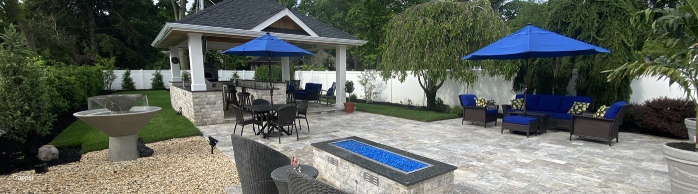 Travertine patio with a linear gas fire table and umbrella-shaded seating below a pavilion